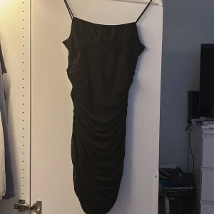 Svart omlottklänning med meshdetaljer - Säljer en svart kortklänning med smala axelband och snygg drapering i mesh över hela klänningen från Shein. Modellen är kort och tight.