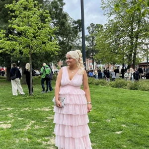Ljusrosa volangklänning med v-ringning - Drömmig långklänning i ljusrosa med flera lager volanger och djup v-ringning. Ärmlös modell med markerad midja och flowy kjol. Perfekt för dig som vill sticka ut på bal eller student. Köp för 1709kr säljer för 900kr. Använd 1 gång
