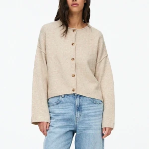 Beige kofta med knappar - Beige kofta i mjukt material med rund halsringning och träfärgade knappar framtill. Modellen är loose fit med långa ärmar och avslappnad passform. Perfekt att slänga över en t-shirt för en chill look.