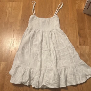 Vit sommarklänning från Subdued - Superfin vit klänning från Subdued med smockad överdel och tunna axelband. Använd endast 2 gånger. Kjolen är volangig och luftig, perfekt för varma dagar. Klänningen har en kort längd och är tillverkad i ett lätt material som känns skönt mot huden. Klänningen är även storlek S/XS