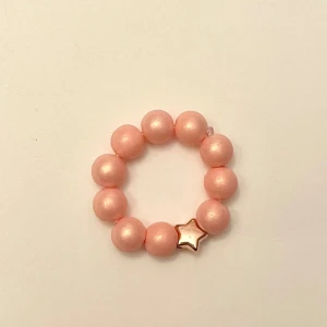 Pärlad ring Rosa korall stjärna - Så söt pärlad ring. Träpärlor och en liten stjärna. Trädd på elastisk tråd så passar de flesta. Perfekt liten accessoar till sommaren! 