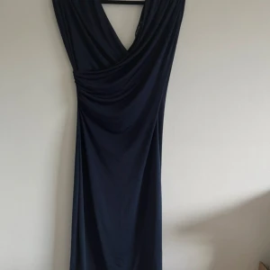 Mörkblå långklänning från NLY One - Snygg mörkblå långklänning från NLY One med djup v-ringning och draperad front. Klänningen har en elegant och enkel design i mjukt, stretchigt material som faller fint längs kroppen. Perfekt för dig som vill ha en stilren look med lite extra edge.