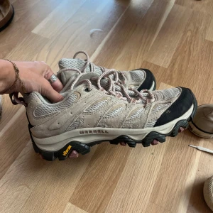 Beige Merrell sneakers med mockadetaljer - Snygga Merrell sneakers i beige med mesh och mockadetaljer. Skorna har kraftig sula med Vibram-gummi för extra grepp och snörning med mönstrade skosnören. Perfekta för dig som gillar outdoor och streetstyle.