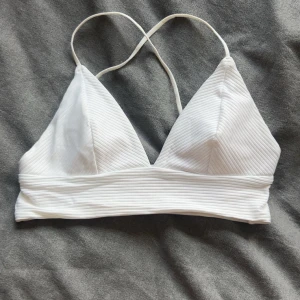 Vit ribbad bikiniöverdel  - Snygg vit bikiniöverdel med ribbad struktur och triangelformade kupor. Smala axelband som korsas i ryggen för en stilren look. Perfekt för stranden eller poolen, enkel att matcha med olika underdelar.