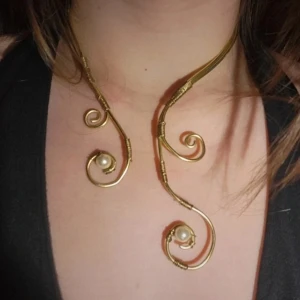 Handgjort Unikt guldhalsband med pärldetaljer - Säljer ett handgjort halsband i guldmetall med spiralformade detaljer och infattade pärlor. Halsbandet har en öppen design som vilar snyggt runt halsen och ger en elegant och konstnärlig look. Guld rostar inte 