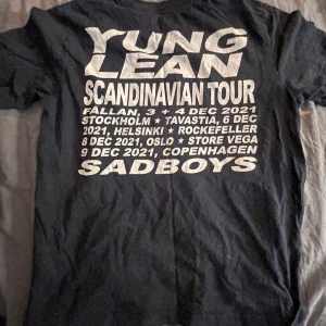 Svart Yung Lean Scandinavian Tour t-shirt - Svart t-shirt från Yung Lean & Sad Boys officiella merchandise med tryck fram och bak. Framsidan har ett porträtt och stjärnor, baksidan har turnédatum och platser från Scandinavian Tour 2021. Perfekt för fans av Yung Lean och Sad Boys.pris kan diskuteras
