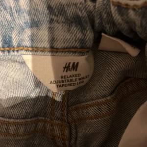 Blå jeans med relaxed passform från H&M - 158 12-13.Säljer ett par blå jeans från H&M med relaxed passform och justerbar midja. Byxorna har avsmalnande ben och klassiska jeanssömmar. Perfekta för dig som gillar en avslappnad stil.