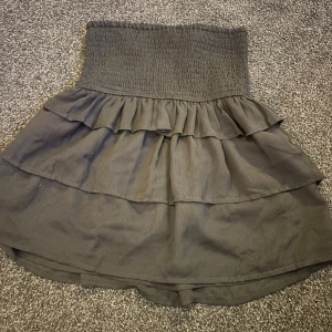 Svart volangkjol med smock i midjan - Säljer en svart kjol med bred smock i midjan och dubbla volanglager. Kjolen är knappt använd i strl 34 skriv om ni har frågor💓.