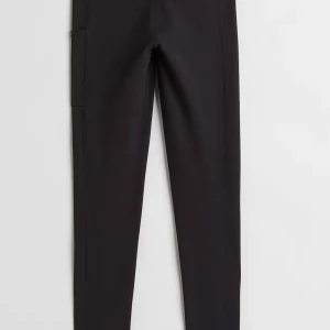 Svarta leggings med sömdetaljer - Säljer ett par svarta leggings med markerade sömmar och tight passform. Byxorna har en minimalistisk design och är tillverkade i ett stretchigt syntetmaterial som sitter skönt mot kroppen. Perfekta för en stilren och sportig look. Även ficka på sidan:) 