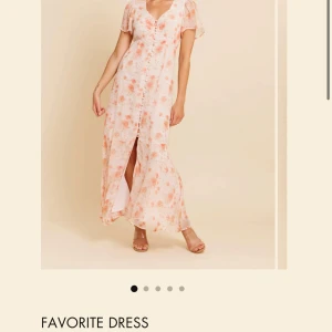 Blommig långklänning med knappar - Ny klänning aldrig använd. Romantisk långklänning med blommigt mönster i ljusa toner och inslag av rosa och orange. Klänningen har korta ärmar, v-ringning, knappar framtill, slits och en öppen ryggdetalj. Perfekt för sommarens tillfällen. Nypris 1699kr 