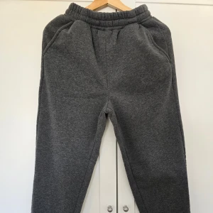 Grå mjukisbyxor med resårmidja - Mysiga grå mjukisbyxor med resår i midjan och sidofickor. Perfekta för chill dagar eller när du vill vara extra bekväm. Klassisk modell med avslappnad passform och mjukt material.