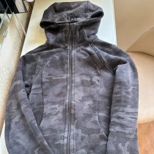 Grå camo hoodie från Lululemon - Säljer en grå hoodie med camouflagemönster från Lululemon. Jackan har dragkedja framtill, huva och en sportig look