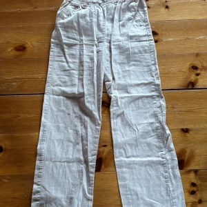 Beiga linnebyxor med resårmidja - Säljer ett par beiga linnebyxor med resår i midjan och raka ben. Byxorna har sidfickor och är tillverkade i ett luftigt linnematerial, perfekta för varma dagar. Passar dig som gillar en avslappnad och enkel stil.