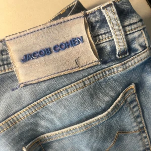 Jacob Cohen jeans - Säljer ett par ljusblå jeans från Jacob Cohën, tillverkade i italien. De är i bra skick men har 1 defekt på själva jeansen(skriv till mig så skickar jag bild). De är annars i bra skick men behöver en tvätt 👍🏼Modellen är Nick 