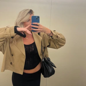 Beige croppad trenchcoat - Säljer en superfin beige croppad trenchcoat. Den har en klassisk design med knappar framtill och långa ärmar. Perfekt för höst och vår när man vill ha något stilrent men ändå avslappnat. Passar perfekt till både vardag och fest!