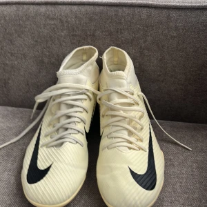 Beige Nike fotbollsskor med svart swoosh - Säljer ett par beige Nike fotbollsskor med högt skaft och svart swoosh på sidan. Skorna har snörning och är designade för bra grepp på planen. Perfekta för dig som vill sticka ut med stilrena skor på matchen.