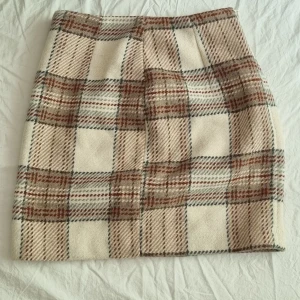 Rutig kjol i ullblandning - Säljer en beige och brun rutig kjol med dragkedja i sidan och innerfoder. Kjolen har en klassisk A-linjeform och är perfekt för dig som gillar retrostil. Mjukt material stl 36 eller S