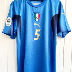 Fabio Cannavaro - Italien VM 2006 - Säljer en klassisk fotbollströja, Fabio Cannavaros matchtröja från VM 2006 när hans Italien vann över Frankrike och blev världsmästare. Tröjan är en remake i nyskick. Aldrig använd. VM-patch.  Large, normal i storleken.  Skickas inom 24 h.  #fotboll