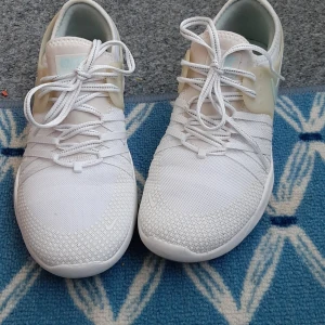 Vita Nike Free sneakers - Snygga vita Nike Free sneakers med mesh-ovandel och ljusbeige detaljer på sidorna. Skorna har snörning och en vit sula med Nike-logga på sidan. Perfekta för en sportig och stilren look. Skor är mycket lätta och bekväma i mycket bra skick. 