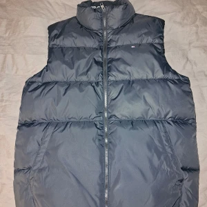 Mörkblå dunväst från Tommy Hilfiger - Snygg Mörkblå padded vest från Tommy Hilfiger med dragkedja framtill och diskret logga på bröstet. Västen har hög krage och två sidofickor med en gömd inner ficka. Fick som present i December men är inte andvänd alls och det finns prislapp, se bilderna😊 Priset kan diskuteras, Skriv gärna👍🏼