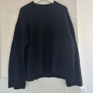 Svart stickad arket tröja  - En enkel och stilren svart stickad tröja med rund halsringning. Tröjan har lång ärm och en något lös passform, perfekt för lager-på-lager under kyligare dagar.