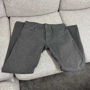 Mörkgrå jeansbyxor från Hugo Boss - Säljer ett par mörkgrå jeansbyxor från Hugo Boss. Klassisk femficksmodell med knapp och dragkedja i gylfen. Snygg och stilren design som passar till det mesta. Märkesdetalj ovanför myntfickan. 34/34.