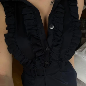 Marinblå klänning med volanger och bälte från Pretty Girl - Säljer en marinblå klänning från Pretty Girl, med krage, volangdetaljer längs knäppningen och ett  bälte i midjan. Säljer då jag aldrig fått tillfälle att använd den! Dvs, aldrig använd-inga defekter.