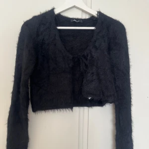 Svart fluffig croppad kofta - Säljer en svart, fluffig och croppad kofta med långa ärmar. Perfekt för att addera lite edge till din outfit. Koftan har en öppen front och är supermjuk.