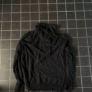 Svart polotröja med dragkedja - Svart polotröja med dragkedja i halsen. Tröjan har långa ärmar och ribbade muddar vid ärmslut och nederkant. Perfekt för kyligare dagar och enkel att matcha med olika outfits.