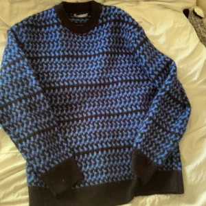 Blå och svart stickad tröja från Zara - Säljer en stickad tröja från Zara i herrstorlek S. Tröjan har ett blått och svart mönster med breda muddar vid ärmslut och nederkant. Perfekt för kyligare dagar och ger en cool, avslappnad look.