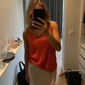 Ribbad orange linnetopp - Säljer en snygg orange linnetopp med ribbad struktur och smala axelband. Perfekt för varma dagar och enkel att matcha med olika underdelar.