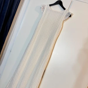 Vit långklänning med spetsdetaljer - Säljer en elegant vit långklänning med fina spetsdetaljer och korta ärmar. Klänningen har en rak och smickrande passform, perfekt för speciella tillfällen. Den är helfodrad och har ett klassiskt, tidlöst utseende.