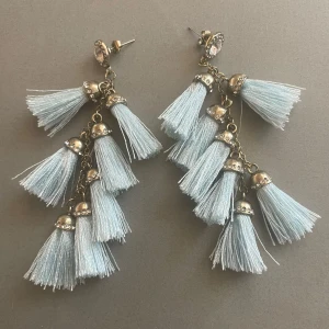 Ljusblå tofsörhängen med strassdetaljer - Säljer ett par statement örhängen med flera ljusblå tofsar i textil och silvriga metalldetaljer med små strasstenar. Perfekta för att lyfta vilken outfit som helst! Är i princip i nytt skick då jag knappt använt dem. 