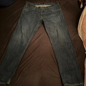 Blå jeansbyxor från Levi's - Klassiska blå jeansbyxor från Levi's med fem fickor och raka ben. Byxorna har normal passform och är tillverkade i slitstarkt denim. Perfekta för dig som gillar tidlös stil och enkelhet. NYSKICK OCH SNABB LEVERANS. Perfekta för en grisch sommar
