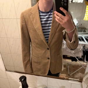 Beige manchesterkavaj - Säljer en beige kavaj i manchester. Klassisk modell med två knappar framtill, fickor och svarta armbågslappar. Perfekt för dig som vill ha en stilren och tidlös look.