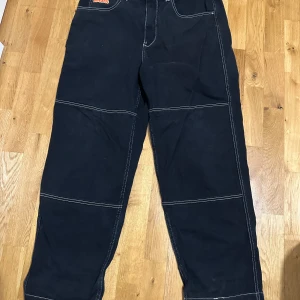 Svarta byxor från GMPIRE med kontrastsömmar - Säljer ett par svarta byxor från empyre med bred passform och vita kontrastsömmar. Byxorna har flera fickor, inklusive en liten ficka fram med broderad logga. Perfekta för dig som gillar streetwear och unik stil.