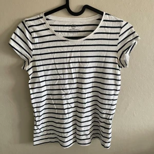 Vit och marinblå randig t-shirt från H&M - Klassisk vit t-shirt med marinblå horisontella ränder från H&M. T-shirten har rund halsringning och korta ärmar. Perfekt basplagg i mjuk bomull som passar till det mesta.