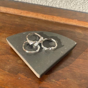 Två silvriga ringar med tvistad design - Säljer två stilrena ringar i silverfärgad metall med tvistad och glansig yta. Perfekta att bära tillsammans eller var för sig för en trendig look. Är ganska rostiga där bak.