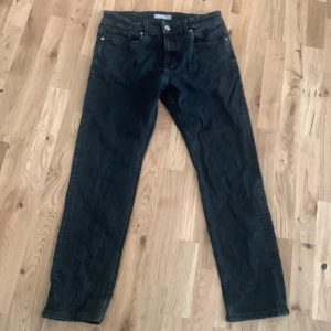 Svarta jeansbyxor med rak passform - Säljer ett par svarta jeansbyxor med klassisk femficksdesign och raka ben. Byxorna har normal passform och stängs med dragkedja och knapp. Perfekta för en stilren och enkel look.