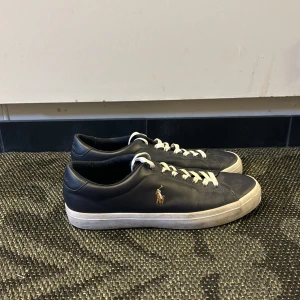 Svarta sneakers från Polo Ralph Lauren - Mörkblåa sneakers från Polo Ralph Lauren med vit sula och vita skosnören. Klassisk låg modell med rund tå och guldfärgad logga på sidan. Perfekta för en stilren vardagslook. Nypris runt 1000 kr, mitt pris 349. Skorna är knappt använda, max två gånger. Pris går att diskuteras! Hör av er vid minsta lilla fundering🤗