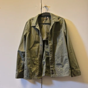 Grön overshirt från Morris - Snygg grön overshirt från Morris med klassisk krage och knäppning framtill. Jackan har tre utanpåfickor och är tillverkad i ett mjukt bomullsmaterial. Perfekt att slänga över en t-shirt för en avslappnad look. Nypris runt 1100 kr, mitt pris 449! Overshirten är knappt använd och är i princip nyskick. Storlek är S men kan även användas som M. Pris går att diskuteras! Hör av er vid minsta lilla fundering🤗