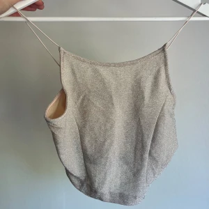 Glittrig croptop - Säljer en glittrig croptop i ljusrosa med tunna axelband. Toppen har en rak halsringning och är ärmlös. Materialet är mjukt och av stretchigt syntet.