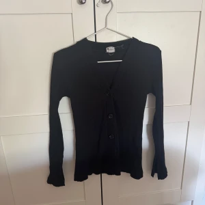 Svart blus - Svart ribbstickad blus i strl S från H&M! Använd fåtal gånger!! Den är figursydd med slits längst ut i ärmarna och går även att använda som en kofta🎀
