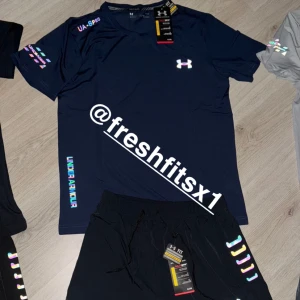 Mörkblå t-shirt och shorts sett från Under Armour - Snygg mörkblå t-shirt från Under Armour med logga på bröstet och färgglada detaljer på ärmar och sidan. Perfekt för träning eller sportiga outfits. Tillverkad i ett lätt och snabbtorkande material.