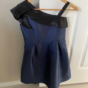 Marinblå klänning med svart ”volang” från Friboo - Super fin marinblå klänning med en off the shoulder design + volang-ish. Klänningen har en vik design på midjan. Perfekt klänning för speciella evenemang för flickor!👗