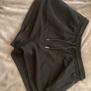 Svarta shorts från H&M med dragsko - Svarta mjuka shorts från H&M med elastisk midja och dragsko. Tillverkade i en blandning av bomull och polyester, perfekta för en avslappnad stil. Klassisk passform och enkel design utan extra detaljer.
