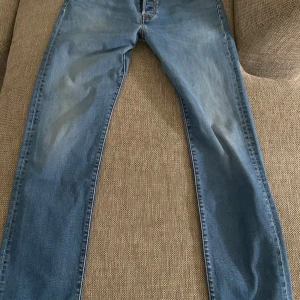 Blå Levis 501 jeans - Klassiska blå Levis 501 jeans med raka ben och normal passform. Byxorna har fem fickor, knappgylf och Levis-lapp bak i midjan. Perfekta för en avslappnad stil och funkar året runt.