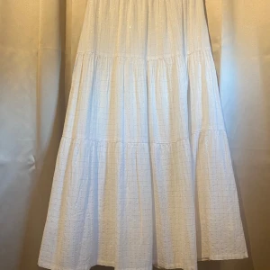 Vit långkjol från Sofie Schnoor - Luftig och flowy vit långkjol från Sofie Schnoor med diskret rutigt mönster i guldtråd. Kjolen har resår i midjan och är tillverkad i bomull och viskos med lite lurex för en lätt glittrig effekt. Perfekt för en somrig look!