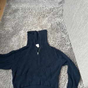 Mörkblå ribbad ziptröja från Monki - Säljer en mörkblå ribbstickad tröja från Monki med halv dragkedja och hög krage. Tröjan har långa ärmar och är i ett mjukt, stickat material. Perfekt för lager-på-lager och enkel att styla till olika outfits.