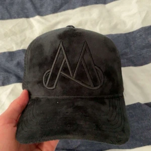 Svart keps från Maggiore med sammetskänsla - Säljer en svart keps från Maggiore med sammetskänsla och broderad logga framtill. Kepsen har mesh på sidorna och justerbar snapback baktill för perfekt passform.